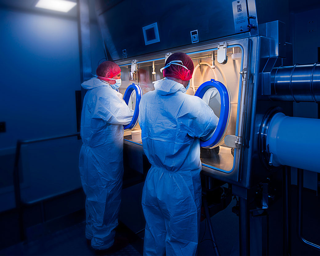 Two people dressed in PPE working in a laboratory environment.