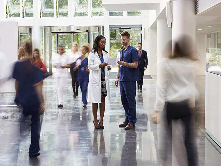 Image of two doctors discussing results in a very busy hospital lobby, medical staff walk around them but are blurred.